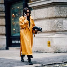 A woman in a yellow coat walks down the road on the phone at London fashion week