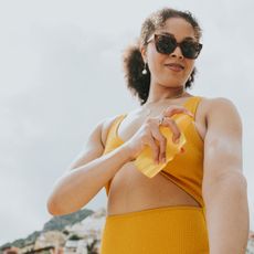 woman in yellow bikini and sunglasses applying sun cream