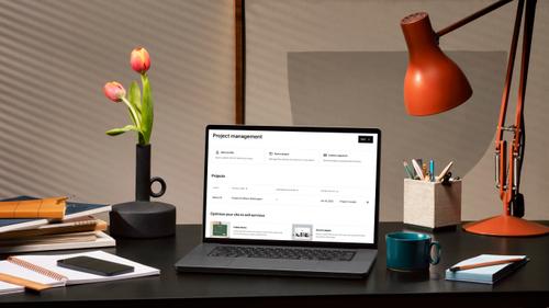 A laptop sitting atop a desk displays the Squarespace project management dashboard, where users can track client communications, send and receive invoices, and monitor the status of all their projects.