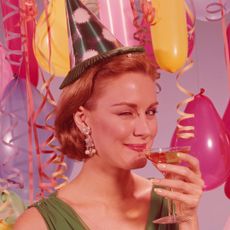 UNITED STATES - CIRCA 1960s: Woman at party, wearing party hat and winking, holding glass of wine.